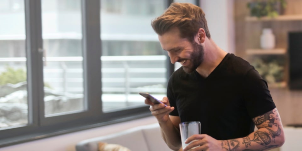 homme sourit en recevant un SMS sur son GSM idée anniversaire couple